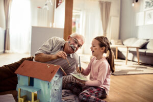 Close up of a little girl painting a dollhouse with her grandfather